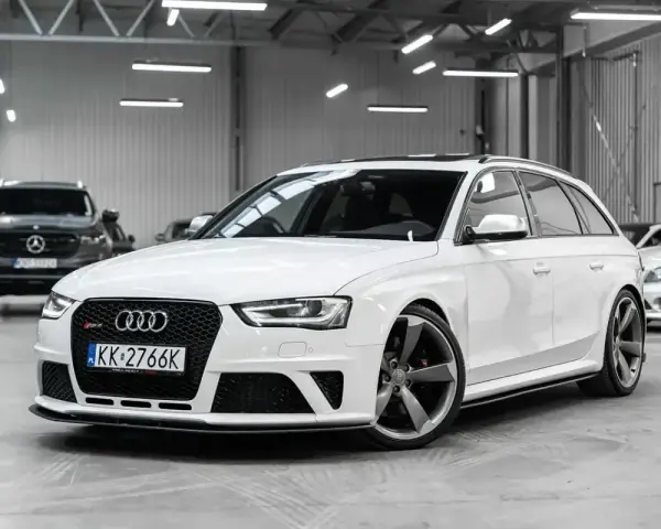 Białe Audi RS4 Avant z przyciemnianymi szybami i sportowymi felgami stoi w garażu.