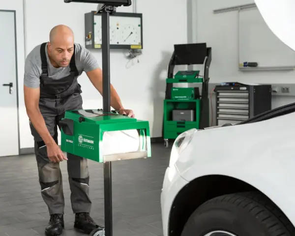 Mechanik dokonuje ręcznej regulacji świateł samochodu za pomocą zielonego urządzenia.