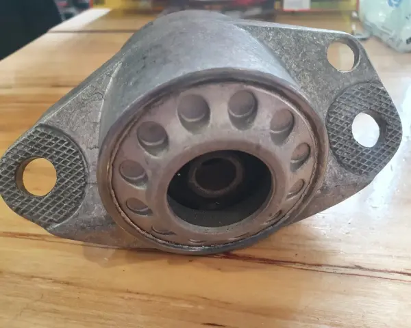Metalowy element zawieszenia auta, przypominający kielichy, leży na drewnianym blacie.