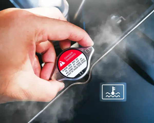 Dłoń dotyka gorącego korka chłodnicy, z którego unosi się para. Widoczny symbol ostrzegawczy i napis "DANGER WARNING". Kuhlmittel stand jest wysoki.