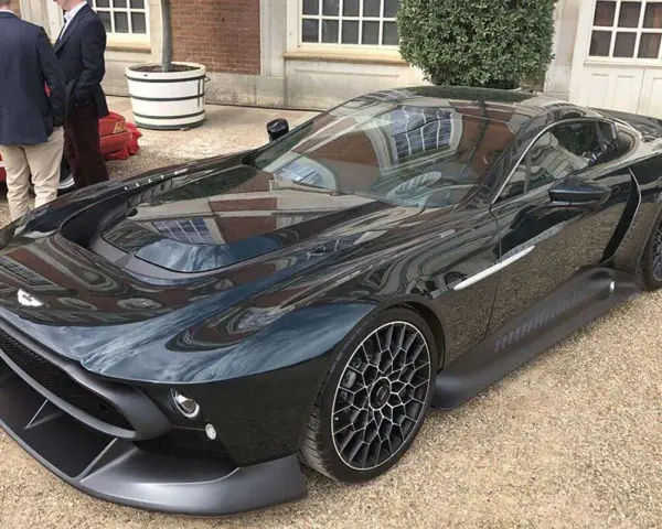 Elegancki, czarny Aston Martin Victor błyszczy na tle ceglanego budynku. Jego aerodynamiczna linia i unikalne felgi przyciągają wzrok.