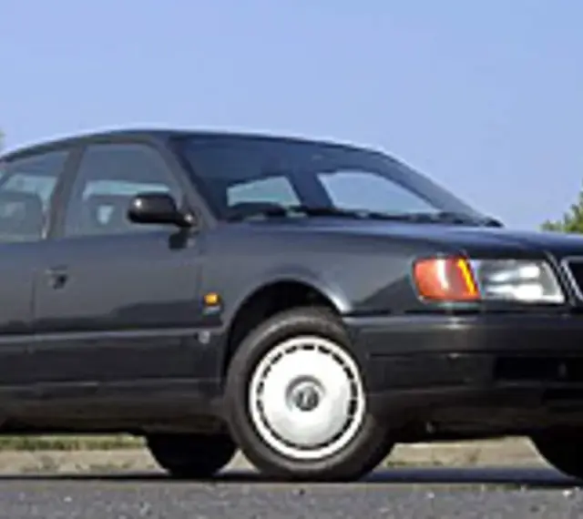 Klasyczny, ciemnoszary Audi A6 C4 z lat 90. stoi na tle błękitnego nieba i zieleni.