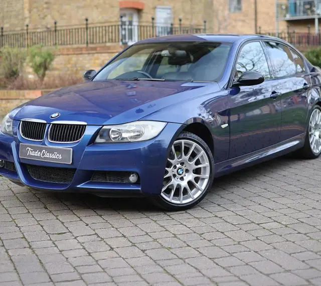 Błękitne BMW 320si z felgami M-pakietu stoi na brukowanym podjeździe.
