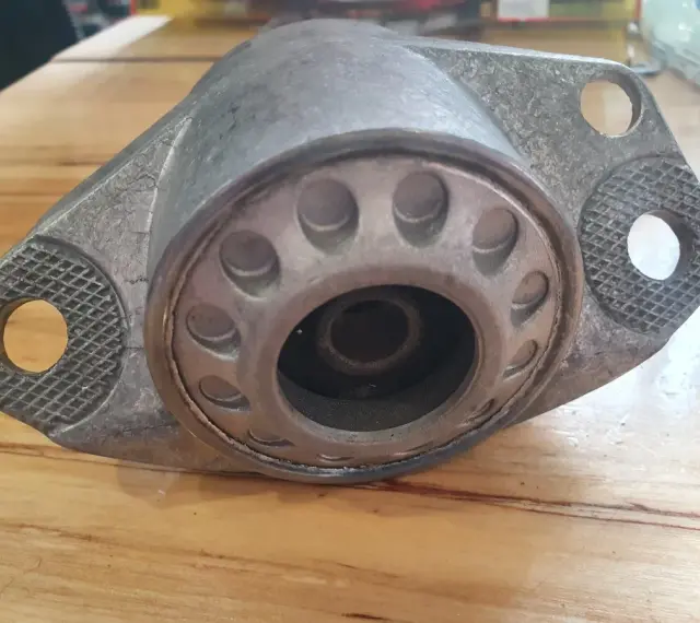Metalowy element zawieszenia auta, przypominający kielichy, leży na drewnianym blacie.