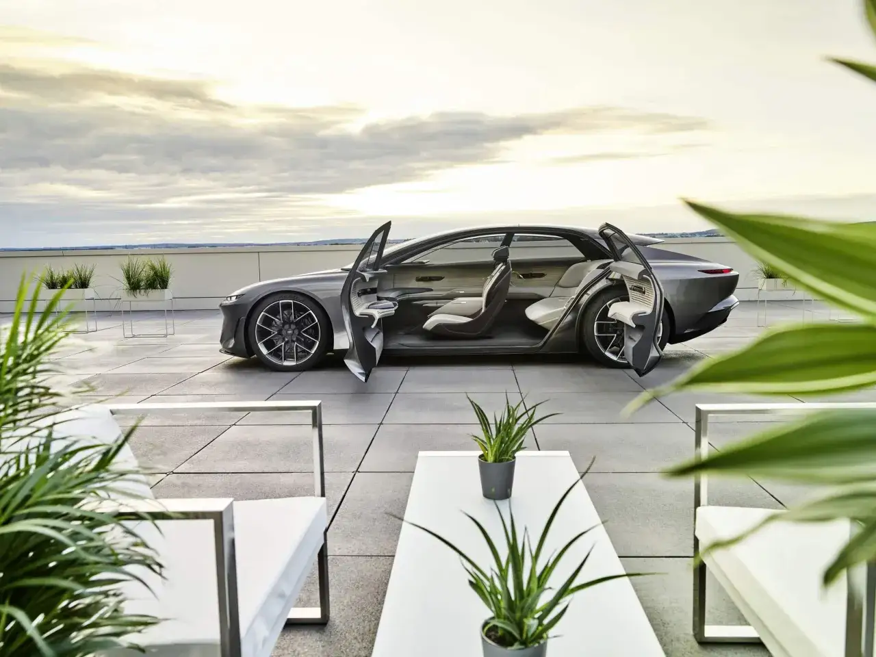 Futurystyczny Audi A9 z otwartymi drzwiami, prezentujący luksusowe wnętrze na tarasie z widokiem na niebo.