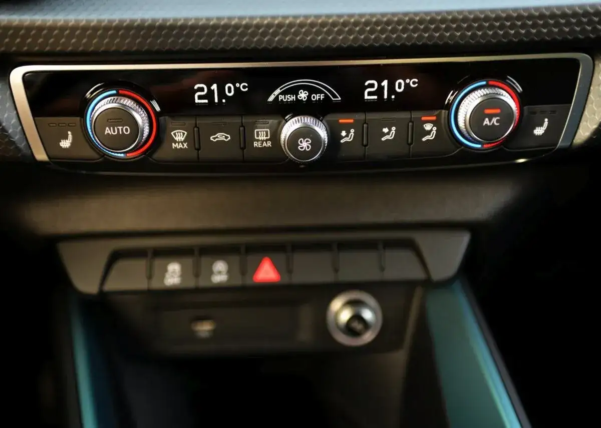 Panel klimatyzacji w aucie z cyfrowym wyświetlaczem temperatury 21°C, pokrętłami regulacji i przyciskami funkcji, w tym obiegu wewnętrznego.