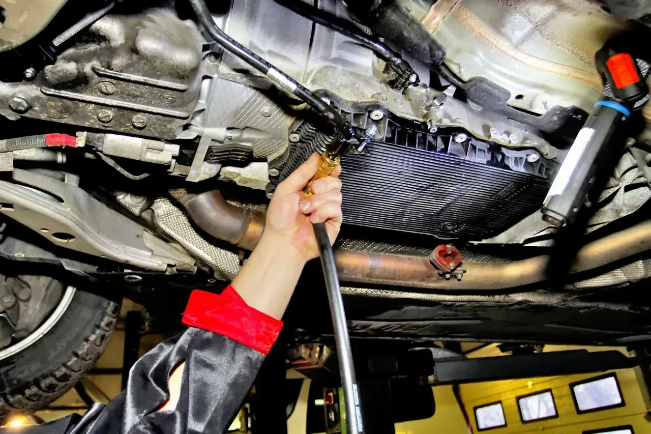 Mechanik wykonuje hyundai i40 wymiana oleju w skrzyni automatycznej. Widać podwozie auta, skrzynię biegów i rękę z narzędziem.