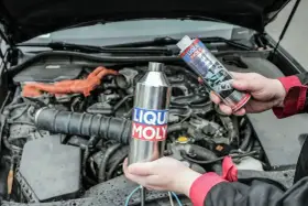 Dwie ręce trzymają produkty Liqui Moly, jeden metalowy, drugi w sprayu, gotowe do czyszczenia katalizatora w silniku samochodu.