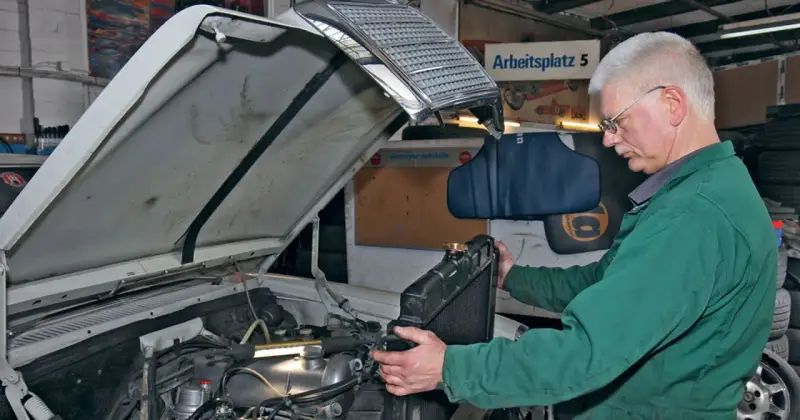 Mechanik w zielonym kombinezonie wykonuje wymianę chłodnicy krok po kroku w warsztacie.