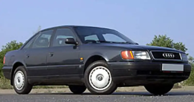 Klasyczny, ciemnoszary Audi A6 C4 z lat 90. stoi na tle błękitnego nieba i zieleni.