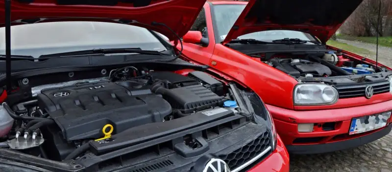 Dwa czerwone Volkswageny z otwartymi maskami. Nowszy model z silnikiem TDI obok starszego, gdzie widać stary diesel.